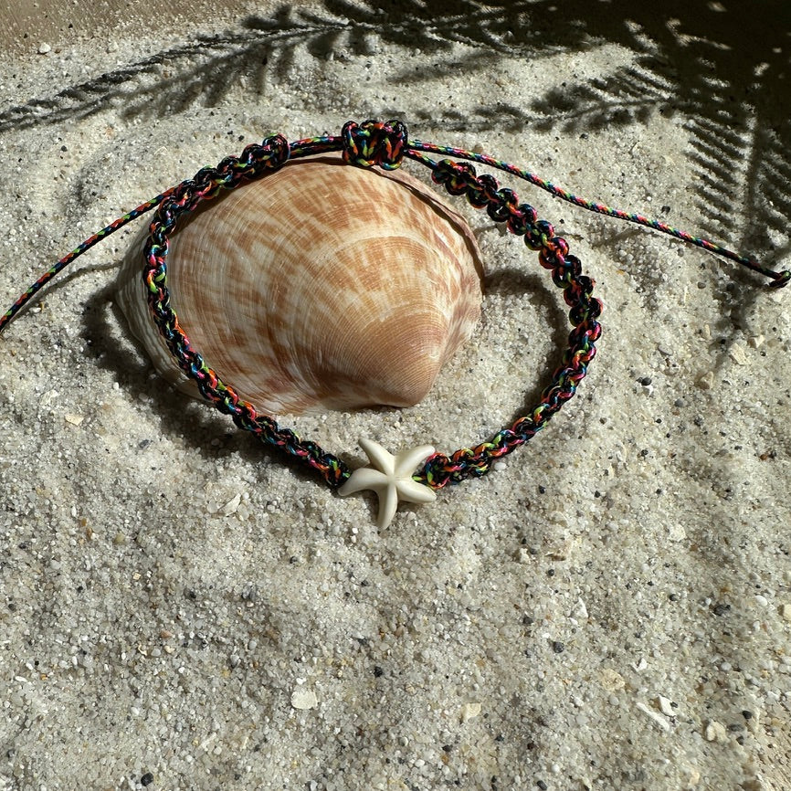 Seestern-Fußkettchen in Schwarz-Neon auf einer Muschel und weißem Sand mit Palmblatt Schatten