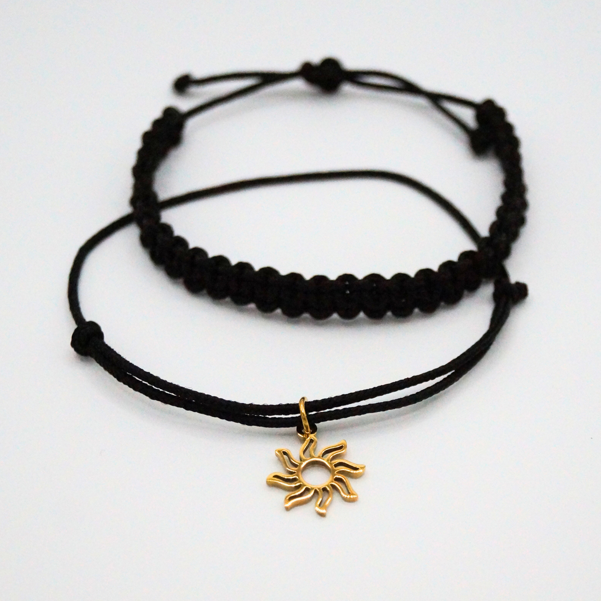 Flatlay eines Armband-Duos in schwarz mit golffarbenem Sonnenanhänger