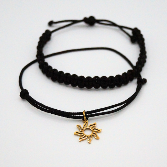 Flatlay eines Armband-Duos in schwarz mit golffarbenem Sonnenanhänger