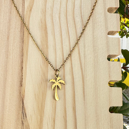 Goldfarbene Edelstahl Halskette mit Palmen Anhänger auf Holzdisplay im Außenbereich.