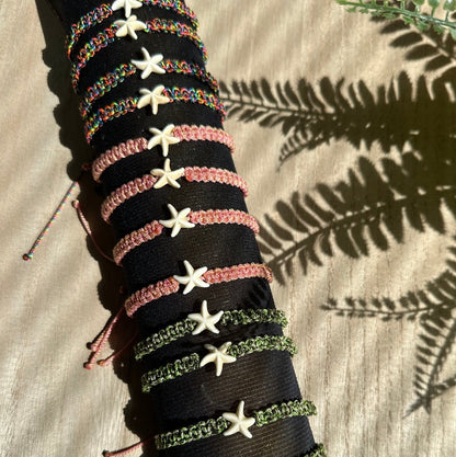 Im Schatten einer Palme sieht man Fußkettchen in 3 verschiedenen Farben auf einem Armbandhalter aufgezogen.
