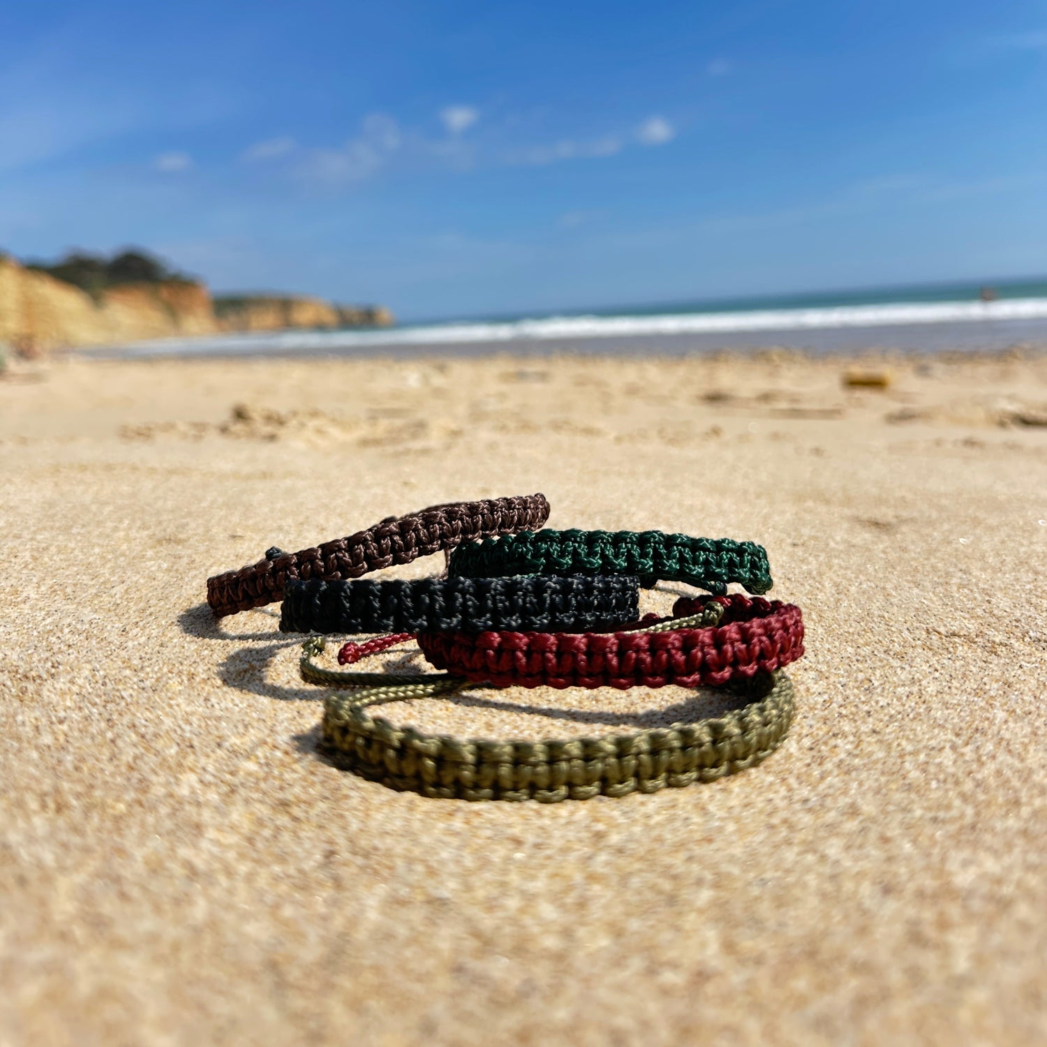 Segeltauarmbänder liegen am Strand in Portugal, man sieht die Klippen und den Atlantik der Algarveküste im Hintergrund