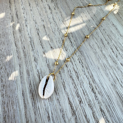 Weiße Kaurimuschel-Halskette mit goldener Edelstahlkette flachliegend auf Holztisch.
