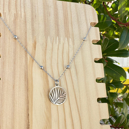 Silberne Edelstahl Kette mit rundem Palmblatt Motiv auf hellem Holzuntergrund.