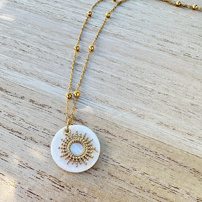 Filigraner goldener Sonnenanhänger auf schimmernder Perlmutt Scheibe.
